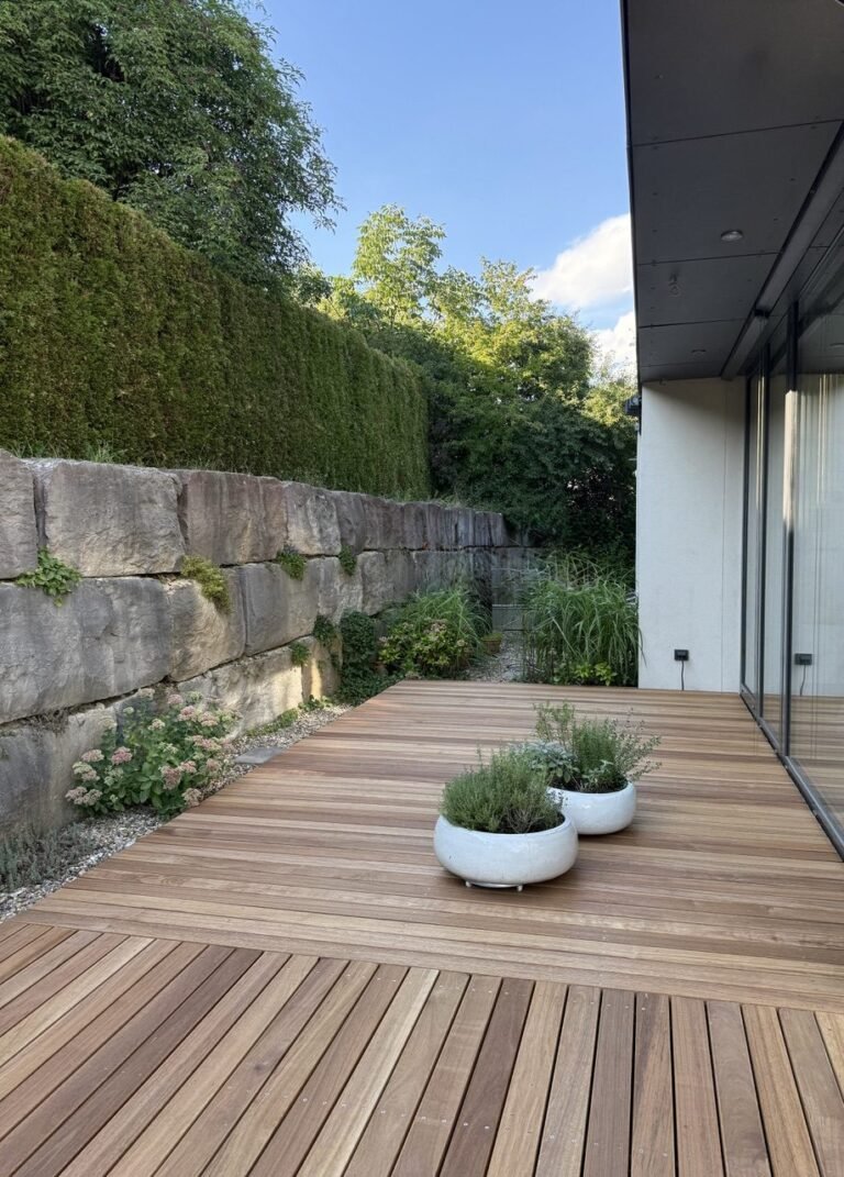 Terrasse aus Guyana Teak entlang einer Natursteinmauer, Blick zum Haus
