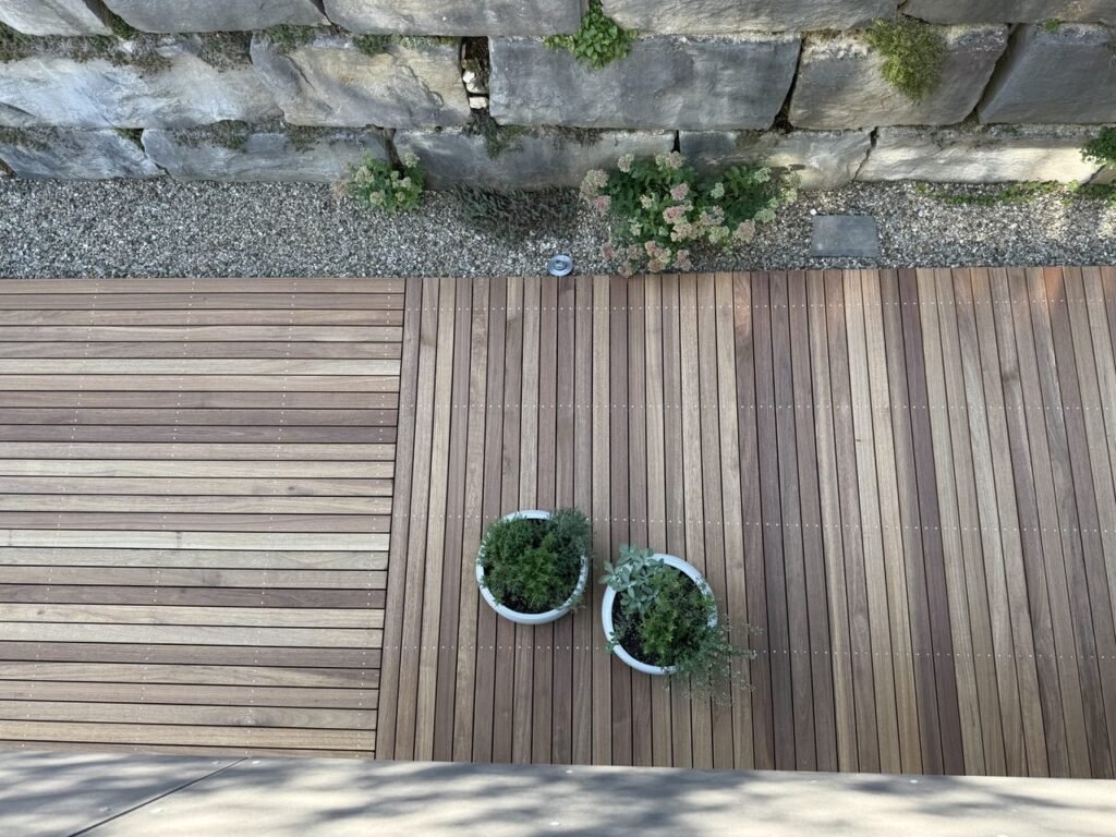 Terrasse aus Guyana Teak 25x90 mm, in zwei Richtungen verlegt, davor eine Natursteinmauer