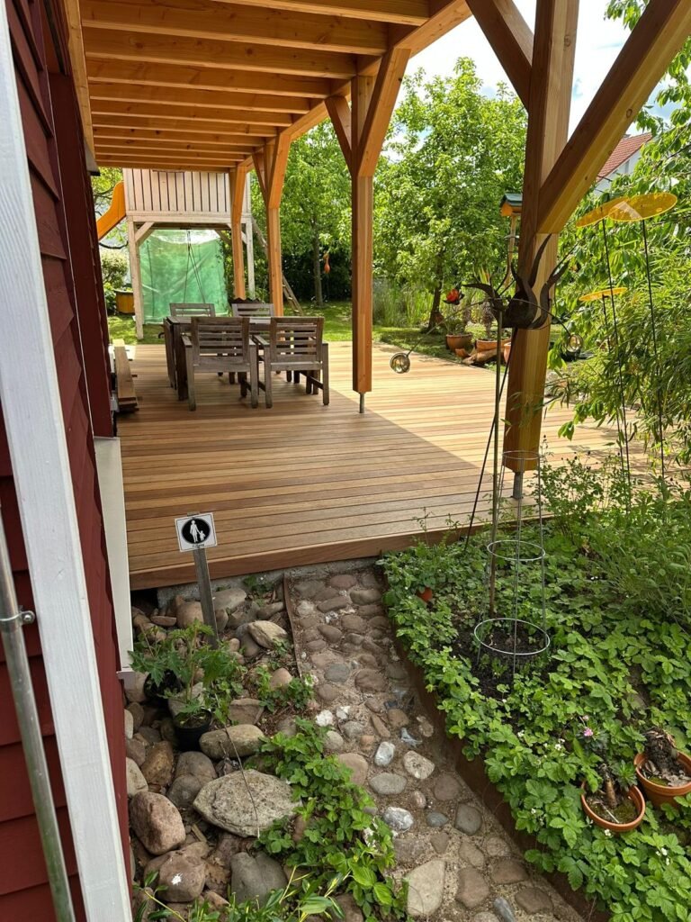 Ueberdachte Terrasse aus Guyana Teak an einem rot gestrichenen Holzhaus