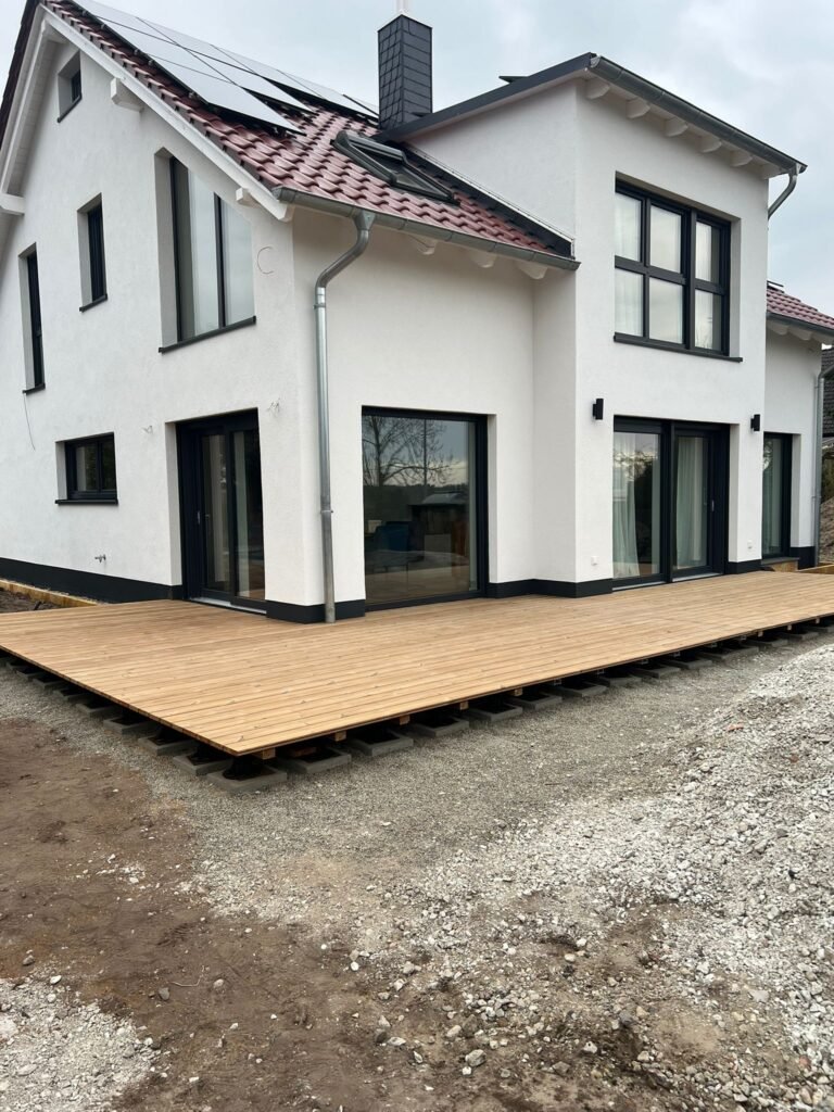 Fertige Holzterrasse an einem weissen Neubau, von der Gartenseite