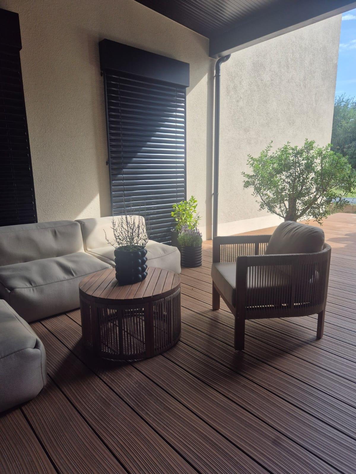 Dunkelbraune WPC-Dielen mit feiner Riffelung, darauf ein helles Outdoorsofa, ein Sessel und ein runder Holztisch