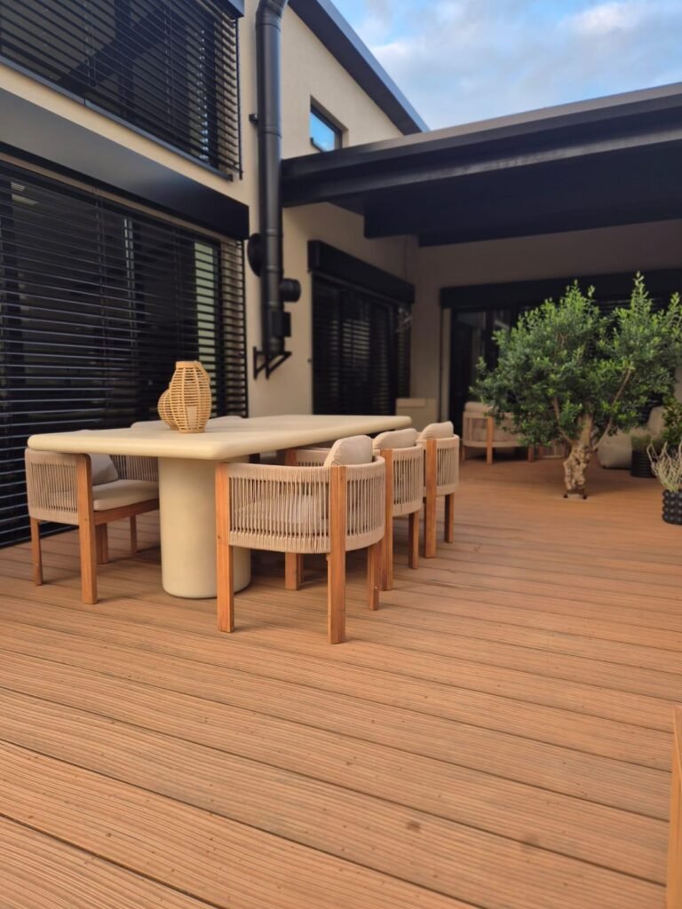 WPC-Terrasse mit Esstisch, Korbstühlen und einem Olivenbaum im Topf am Ende der Fläche